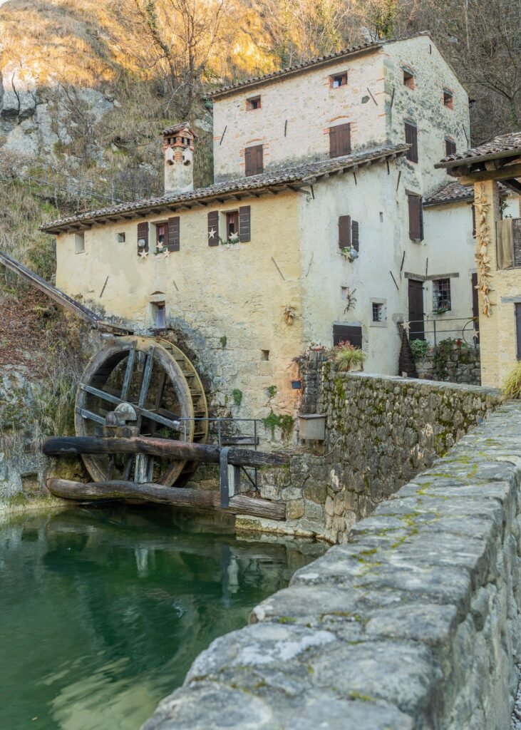 Charming historic watermill with stone walls and a water wheel by a scenic riverbank.